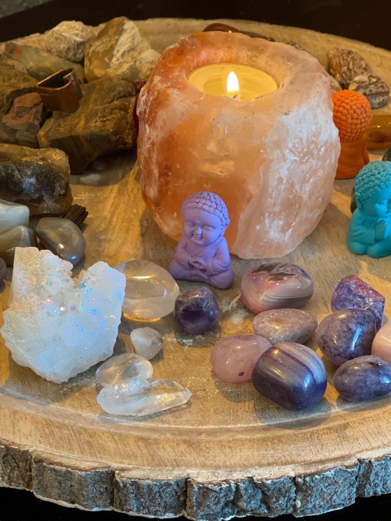 crystals and baby Buddha sitting next to Himalayan salt candle